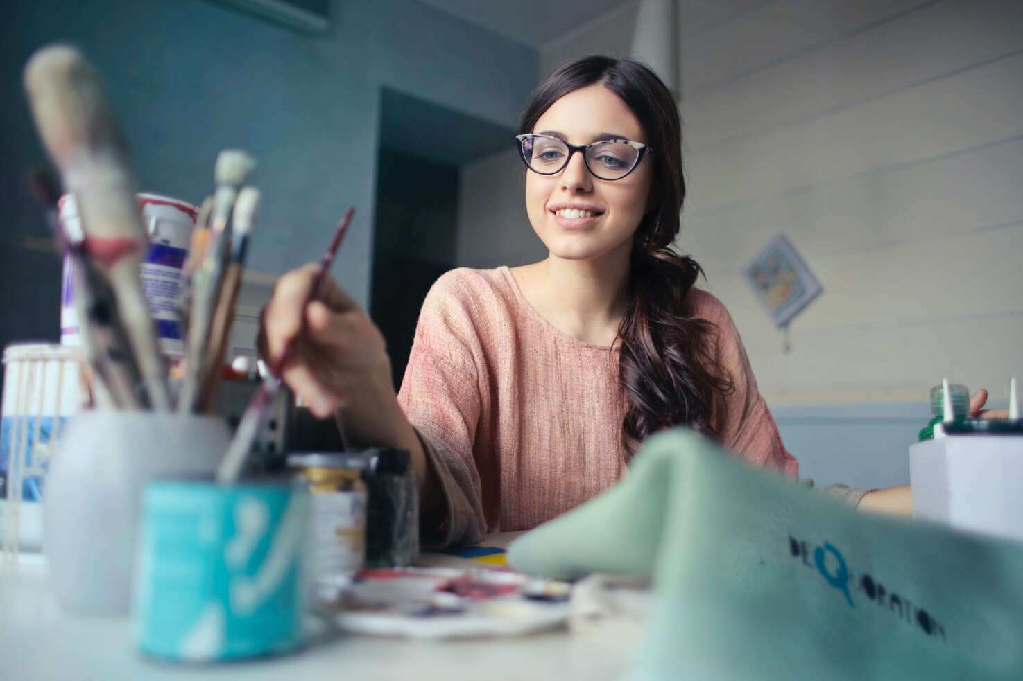 A woman with glasses holding a paintbrush.